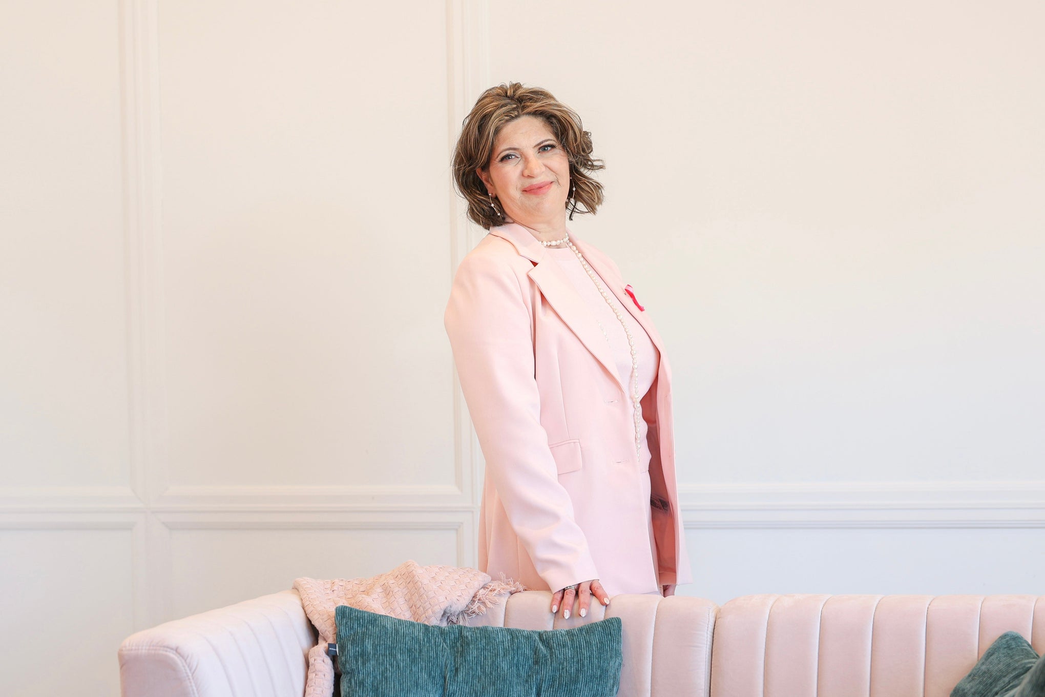 Woman standing behind a sofa with decorative pillows against a white wall