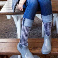 model wearing medi rejuva compression sock in houndstooth black and white colour, sitting on a wodden bench