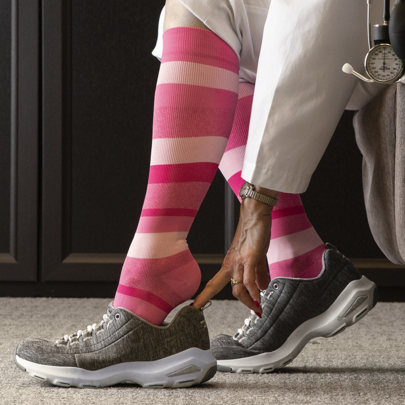 nurse sitting on a chair putting on the sigvaris microfibre pattern compression sock in pink stripe