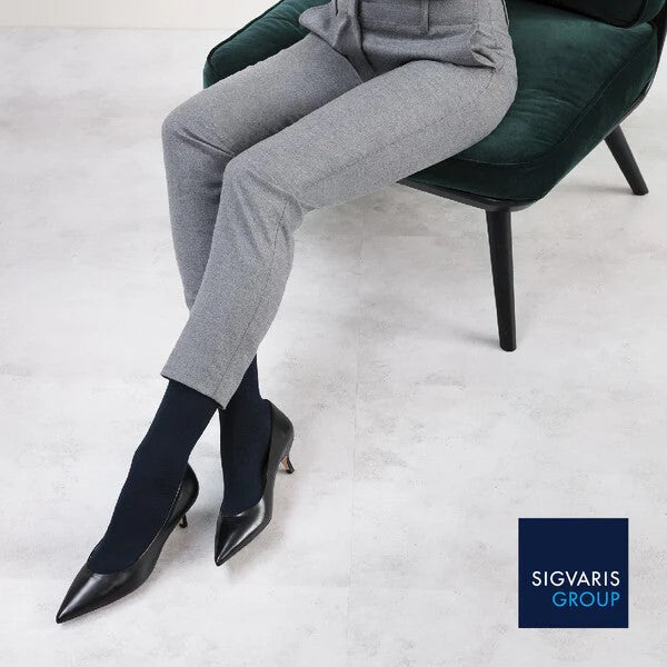 woman sitting on work chair waering black sigvaris sea island compression sock in grey trouser