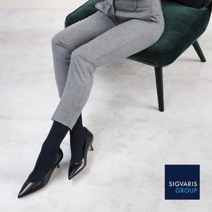 woman sitting on work chair waering black sigvaris sea island compression sock in grey trouser