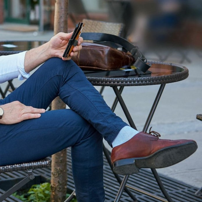 Man sitting at an outdoor café wearing denim colour linen compression sock by Sigvaris, with navy trousers and brown dress shoes.