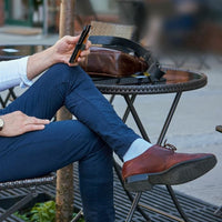 Man sitting at an outdoor café wearing denim colour linen compression sock by Sigvaris, with navy trousers and brown dress shoes.