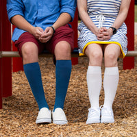 Two models sitting in the park. Left model is a male wearing the sigvaris 262 bamboo compression sock in stone blue, and the right model is a female who is also wearing the sigvaris bamboo compression sock in Ivory.