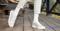 close-up of woman's leg sitting on a patio chair wearing a white sigvaris cushioned cotton compression sock