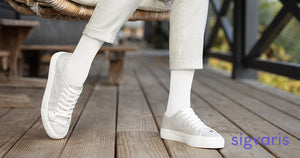 close-up of woman's leg sitting on a patio chair wearing a white sigvaris cushioned cotton compression sock