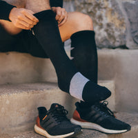 person sitting on outdoor concrete steps, pulling up a black sigvaris athletic recovery compression sock.