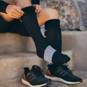 person sitting on outdoor concrete steps, pulling up a black sigvaris athletic recovery compression sock.