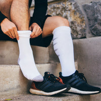 person sitting on outdoor concrete steps, pulling up a white sigvaris athletic recovery compression sock.
