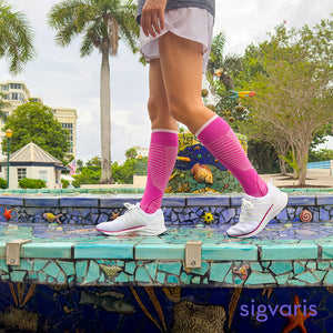 woman wearing sigvaris motion flow tech compression sock in orchid, walking on the edge of a colourful fountain