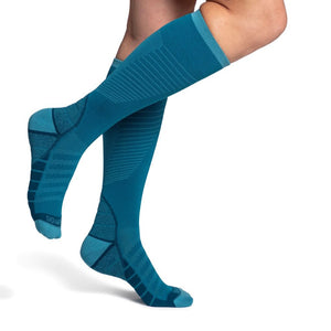 model wearing sigvaris flow tech compression sock in teal, side view.