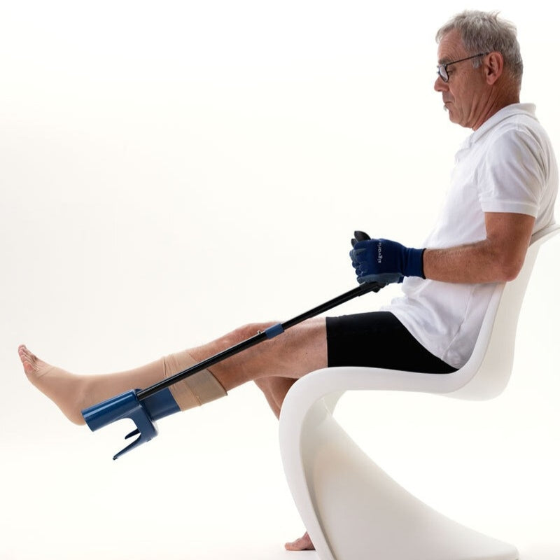 elderly man sitting on a chair using the sigvaris melony donning aid to put on a compression sock, wearing donning gloves for support