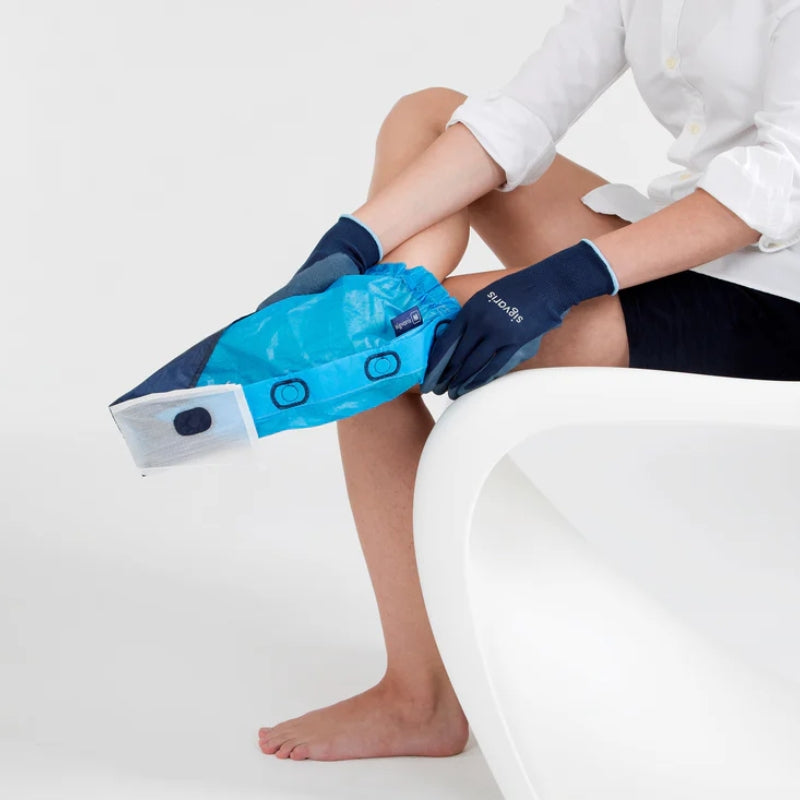 person sitting on a chair using the sigvaris magnide donning aid to assist in putting on compression socks while wearing donning gloves.