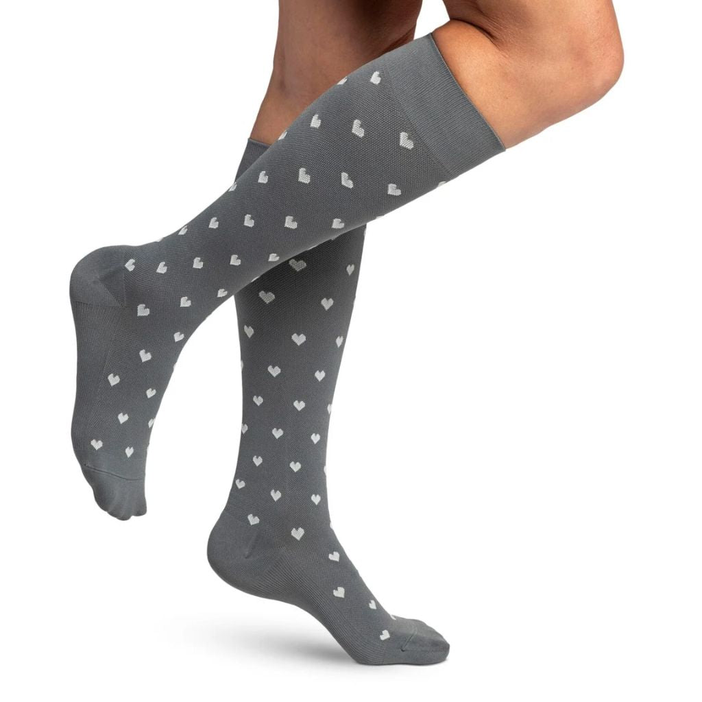 woman model wearing sigvaris microfibre pattern compression sock in grey hearts, side view.