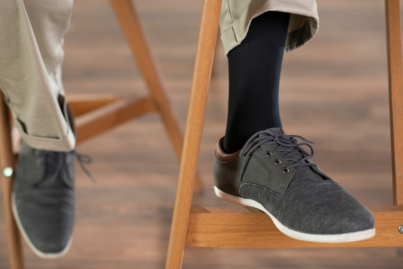 man wearing black sigvaris opaque compression socks with khaki pants and dark shoes, sitting on a wooden stool