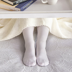 woman sitting on the bed wearing white sigvaris essential cotton compression sock while reading a book