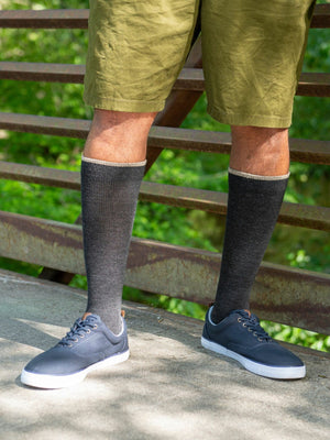man on a wooden bridge wearing the sigvaris merino wool outdoor compression sock in charcoal