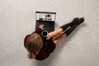 woman wearing the sigvaris merino outdoor knee high compression sock in olive, while working on a laptop and drinking coffee.